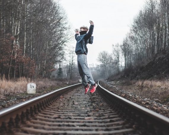 man in black jacket and blue denim jeans walking on train rail during daytime