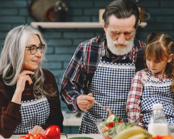 Grandparents and granddaughter preparing salad in home kitchen, creating memories together.